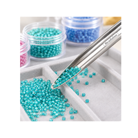 Beadalon stainless steel bead scoop collecting turquoise seed beads from a beading tray, with colourful bead containers in the background