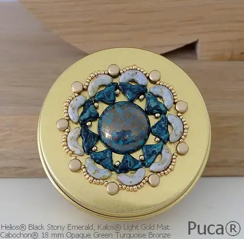 Decorative round compact with gold and gemstone design on a wooden surface, featuring Puca brand.