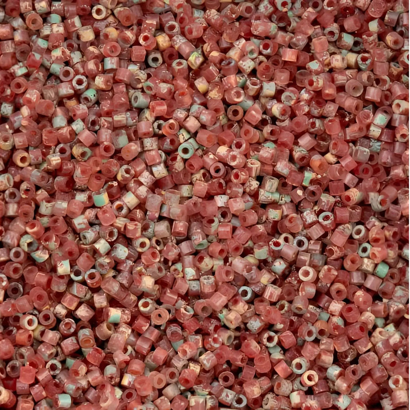 A dense pile of small cylindrical seed beads in a dusty rose red color, with some showing light blue-green and cream accents.