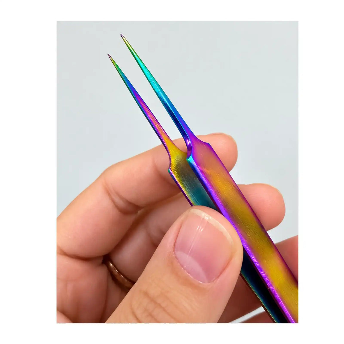 Close-up of Chroma Series rainbow titanium-coated fine point tweezers held in a hand, showing the precision tips and colourful finish