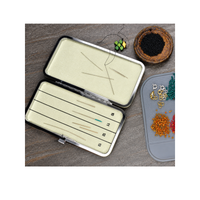 Open double-sided magnetic needle case holding beading needles on a jewellery-making workspace with seed beads, thread and jewellery findings