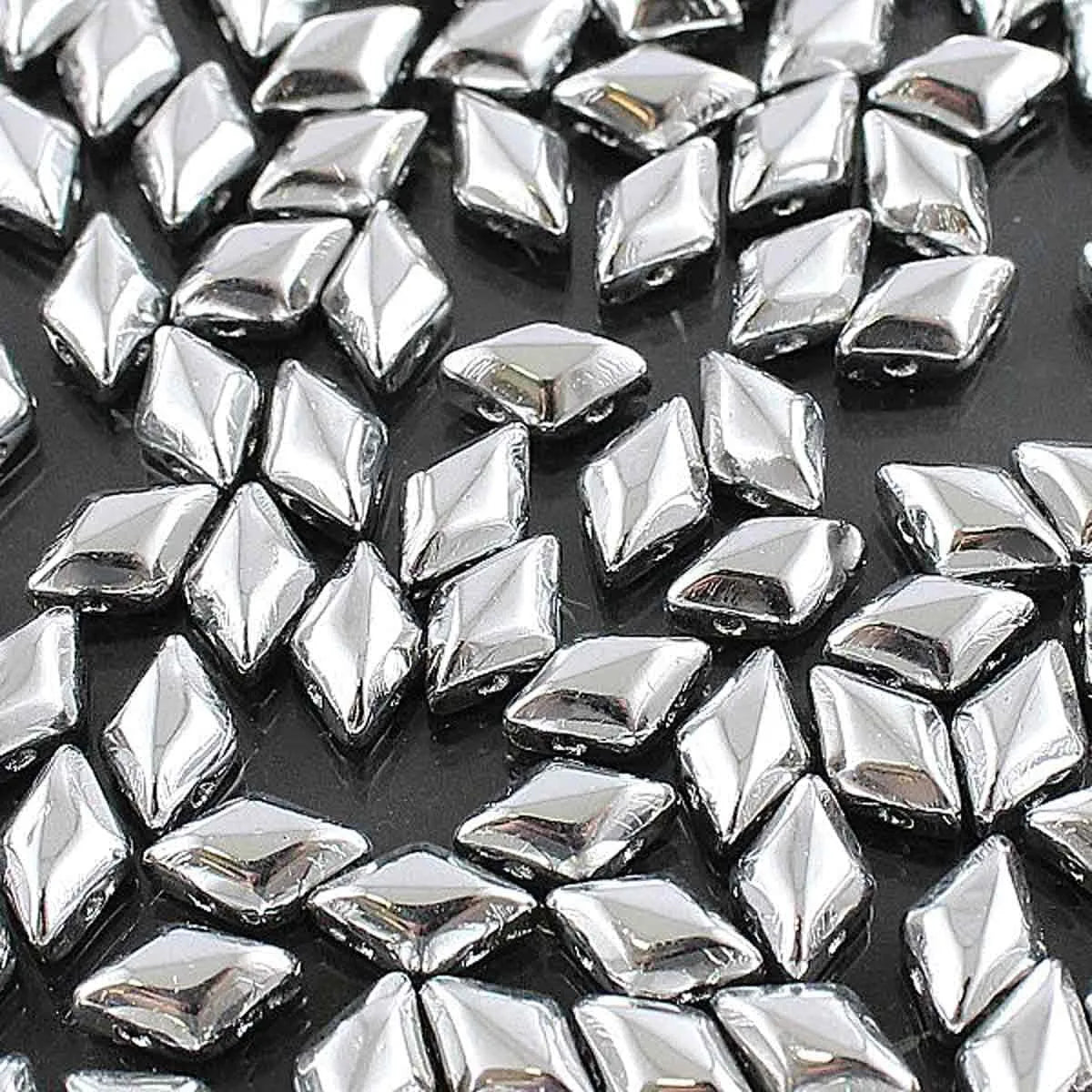 Close-up of shiny silver diamond-shaped craft beads scattered on black surface