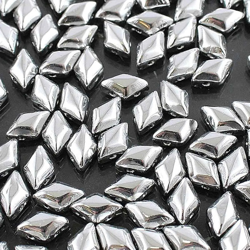 Close-up of shiny silver diamond-shaped craft beads scattered on black surface