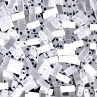 Close-up of numerous translucent rectangular beads with two holes, scattered on a dark surface