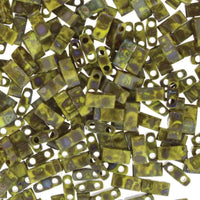 Close-up of yellow-green two-hole rectangular glass beads with iridescent finish scattered on white background