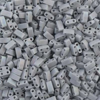 Close-up of numerous small gray two-hole rectangular spacer beads scattered uniformly