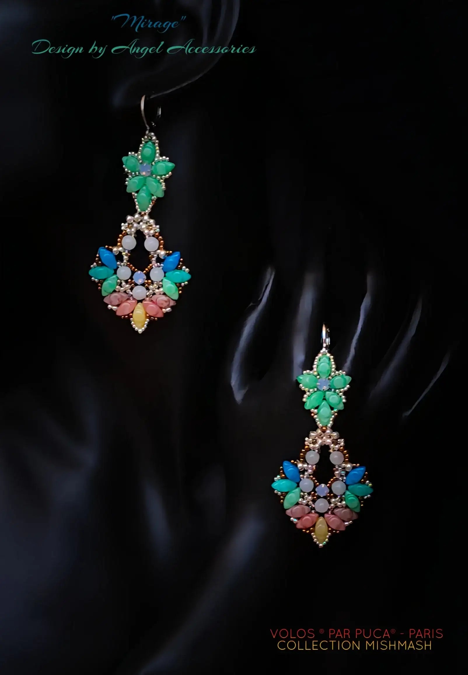 A pair of ornate dangling earrings displayed on a black mannequin hand against a dark background. The earrings feature a green floral top, a central cluster of turquoise, blue, white, and pink stones, and a gold-toned lower section with yellow and pink flower-like accents.