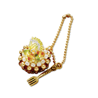 A gold-tone chain accessory with a decorative pendant featuring faux pearls, brown beads, and a small cartoon character, plus a dangling gold-tone fork charm, shown on a plain white background.