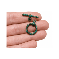 Green metal toggle clasp on a hand against a white background