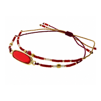 A beaded multi-strand cord bracelet with a prominent oval red stone in a gold bezel setting, accented with red, white, and gold beads on a white background.