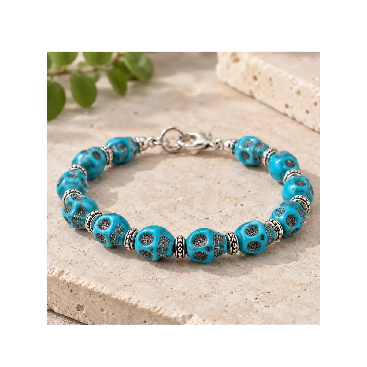 A turquoise and silver beaded bracelet displayed on a textured beige stone surface with a blurred green plant in the background.