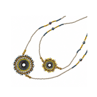 Two beaded necklaces displayed on a clean white background. One necklace features a larger circular pendant with a black and yellow sunburst design surrounded by blue, white, and gold beads.