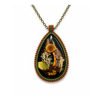 Teardrop-shaped pendant with nature-themed design on a white background